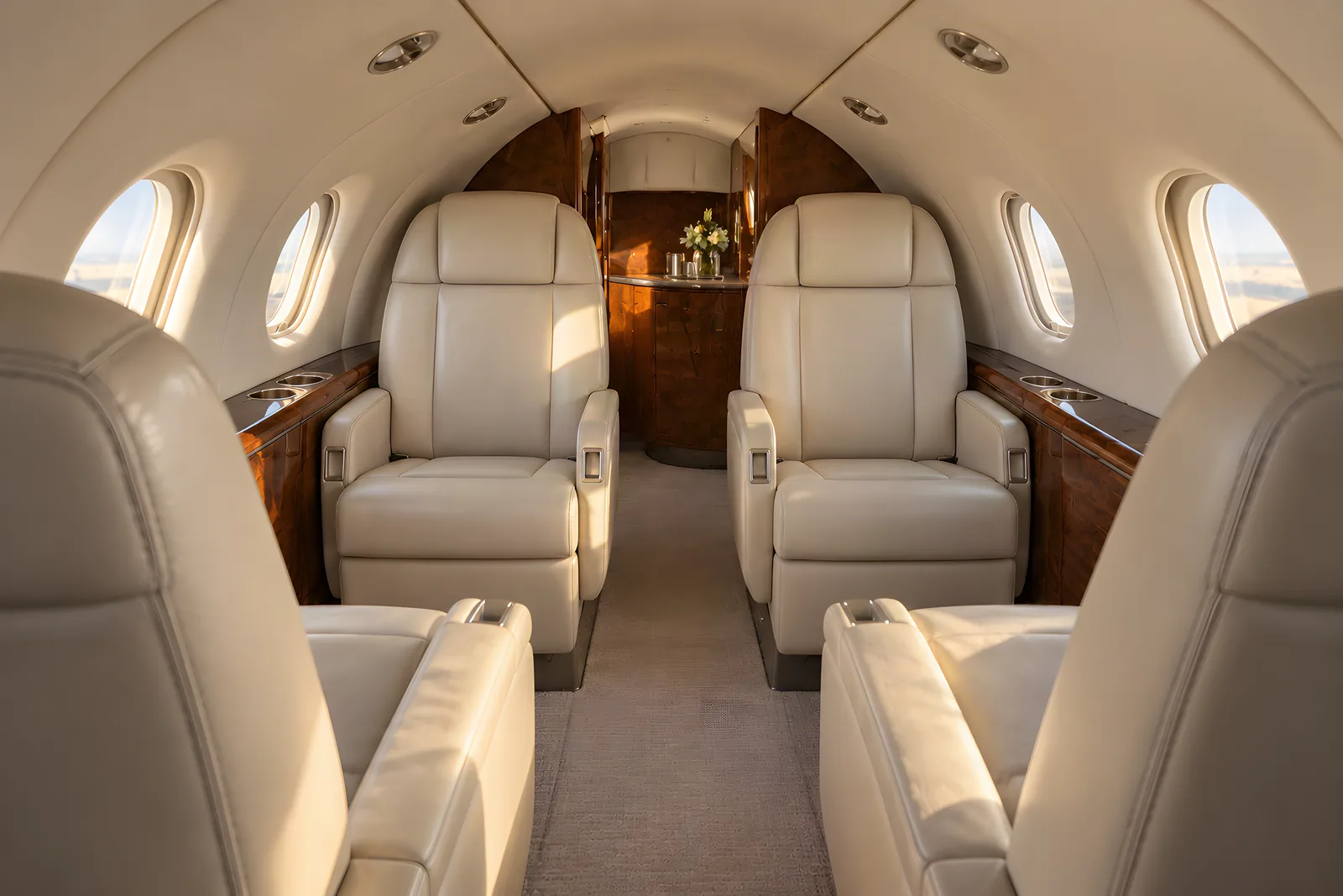 Beechcraft Premier I cabin interior illustration: an eye-level view looking aft through the compact Beechcraft Premier I cabin shows six cream leather seats, three oval windows on each side, walnut veneer and a low curved ceiling in warm natural light.