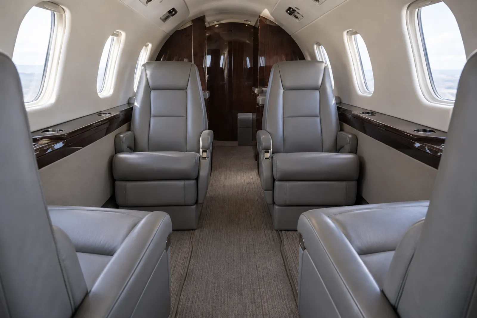 The cabin of a Citation CJ4, looking aft past four gray leather club seats