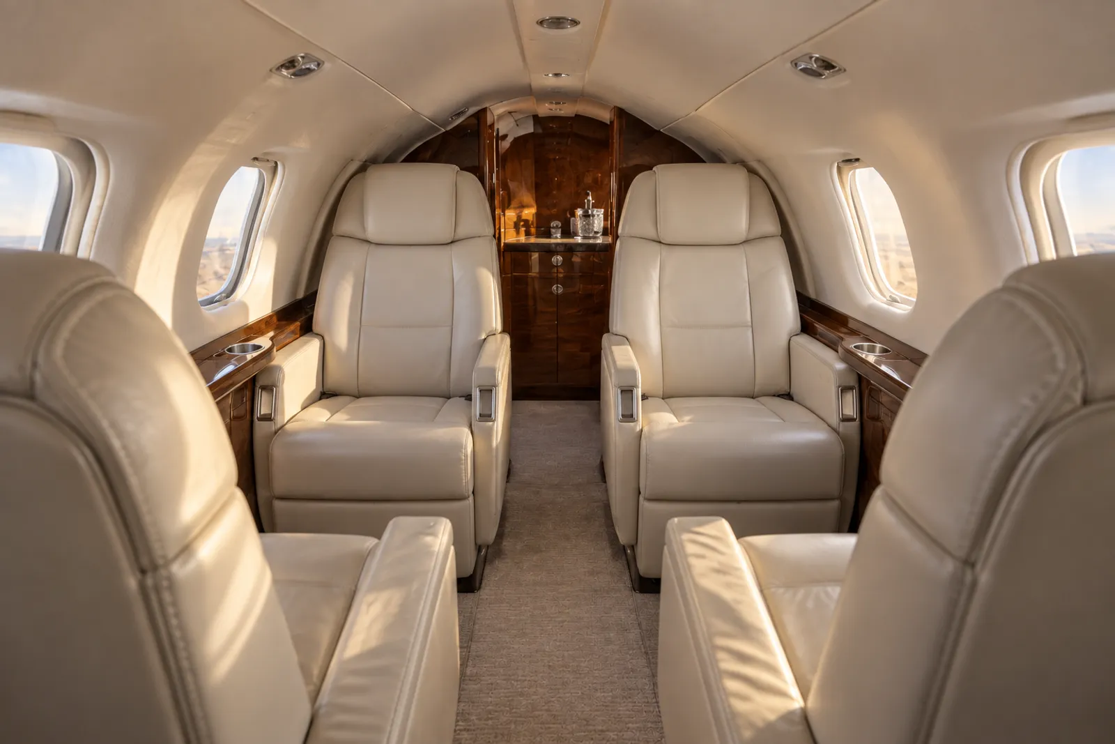 Warm natural light illuminates three cream leather seats, wood trim and rounded windows in the low, narrow Eclipse 500 cabin viewed aft from seated eye level.