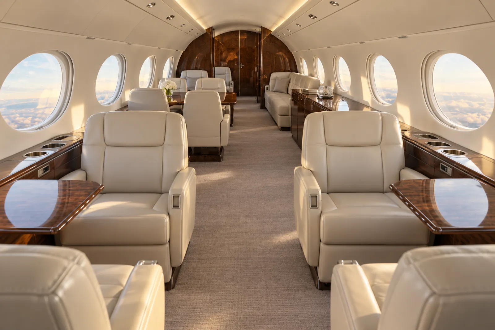 An eye-level view looking aft through a Gulfstream V stand-up cabin shows cream leather club chairs, a wood conference table, an aft divan and large oval windows in warm natural light.