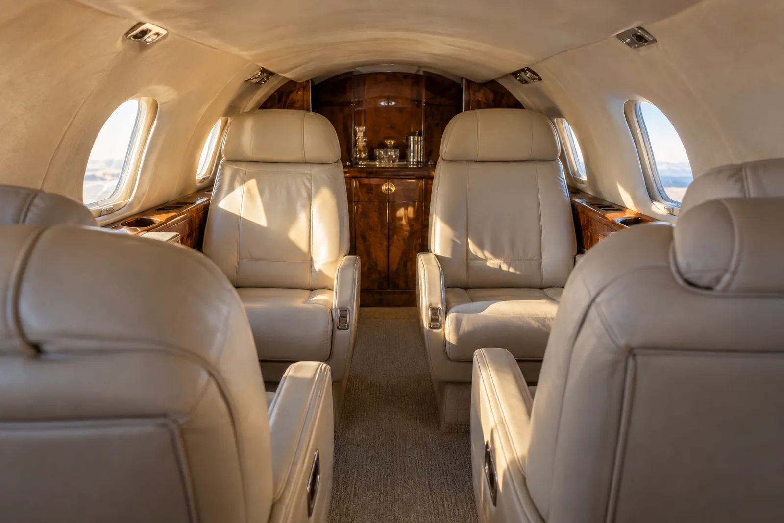 Warm natural light illuminates the Learjet 35A's low, narrow cabin with cream leather club chairs, a three-place rear bench, small oval windows and polished wood veneer.