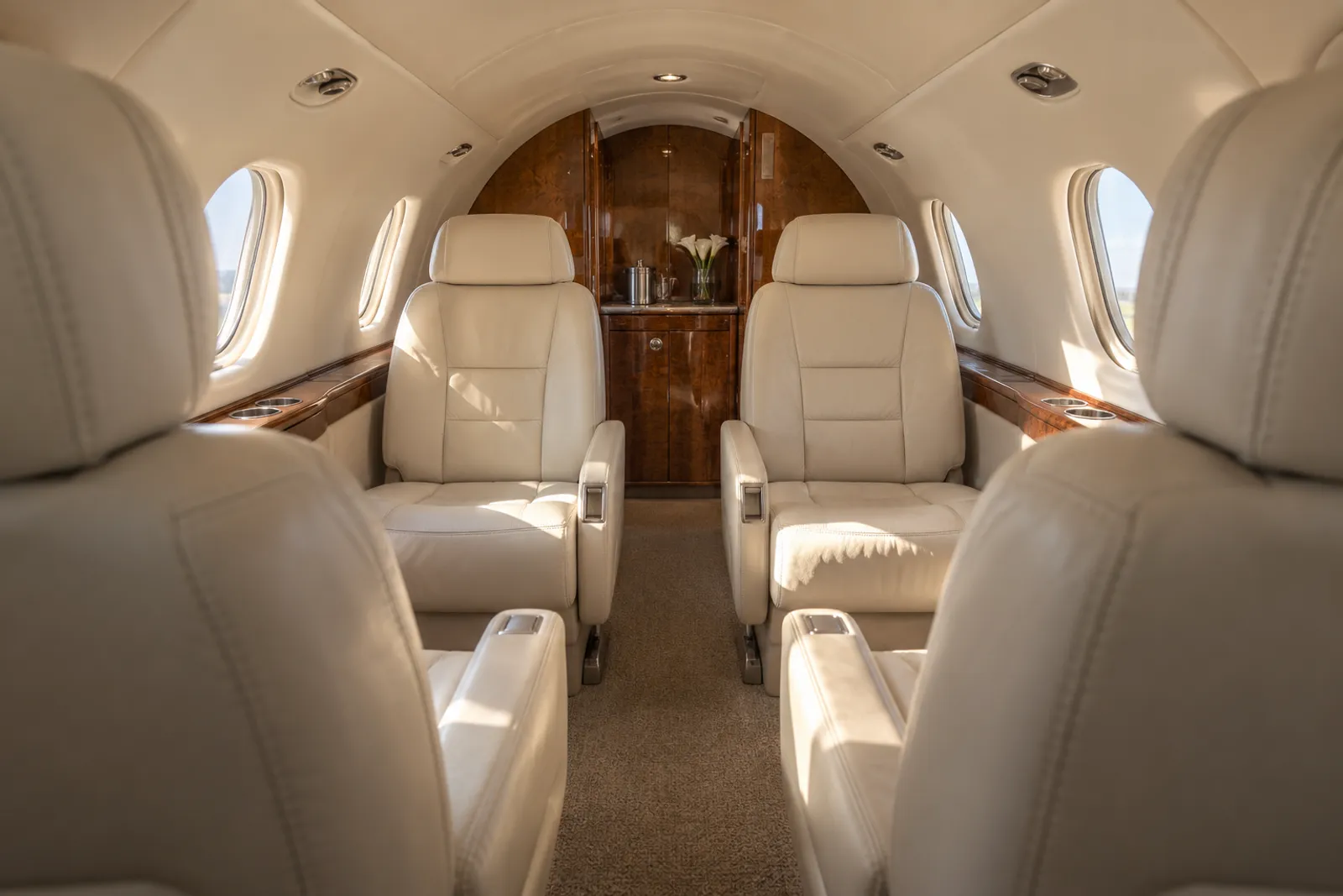 Warm daylight fills the low, narrow Nextant 400XTi cabin, with cream leather divan and club seating, oval windows, walnut cabinetry and a flat aisle leading aft to the lavatory.