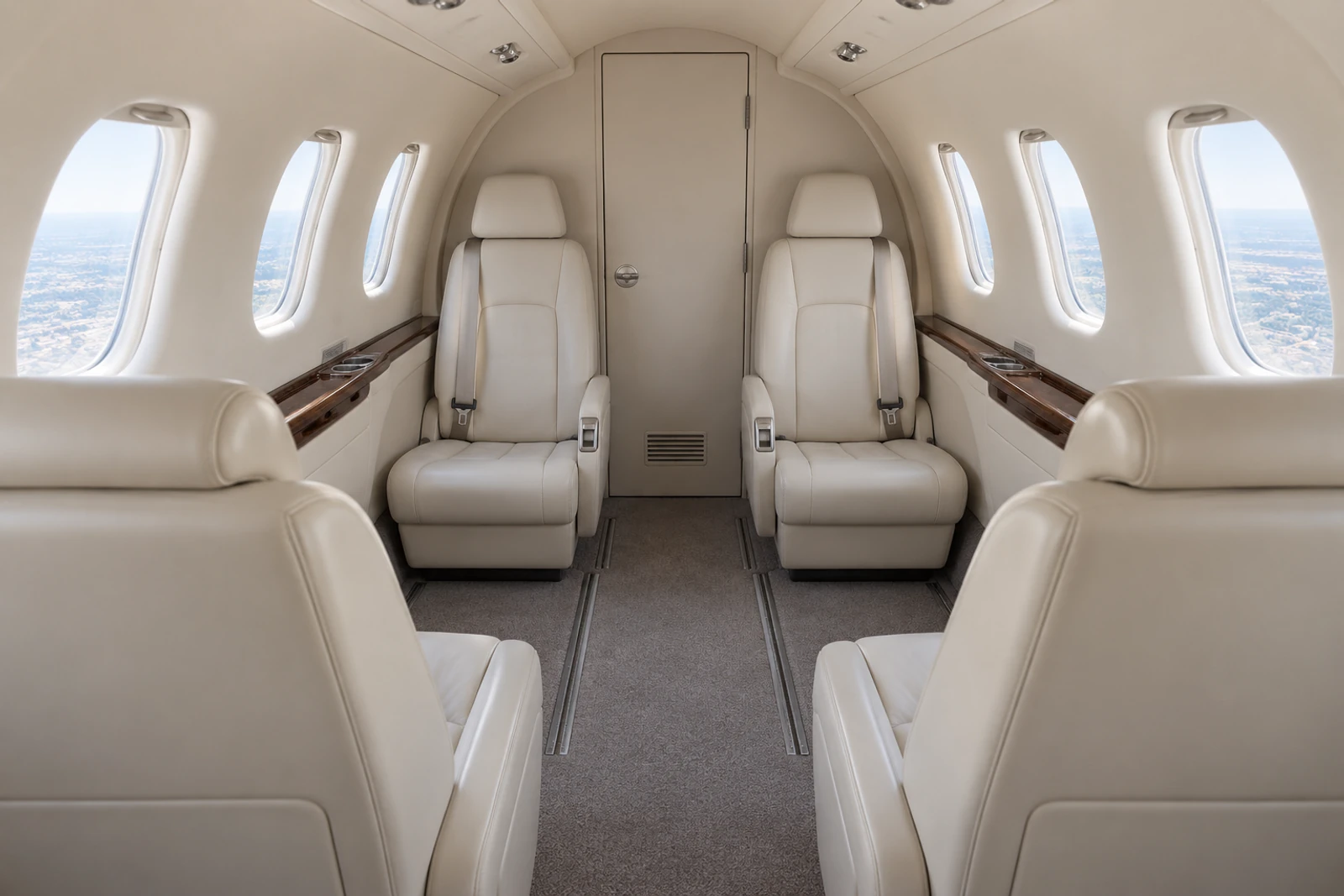 Representative baseline Phenom 100 cabin looking aft at four club chairs and closed lavatory door; actual interiors vary.