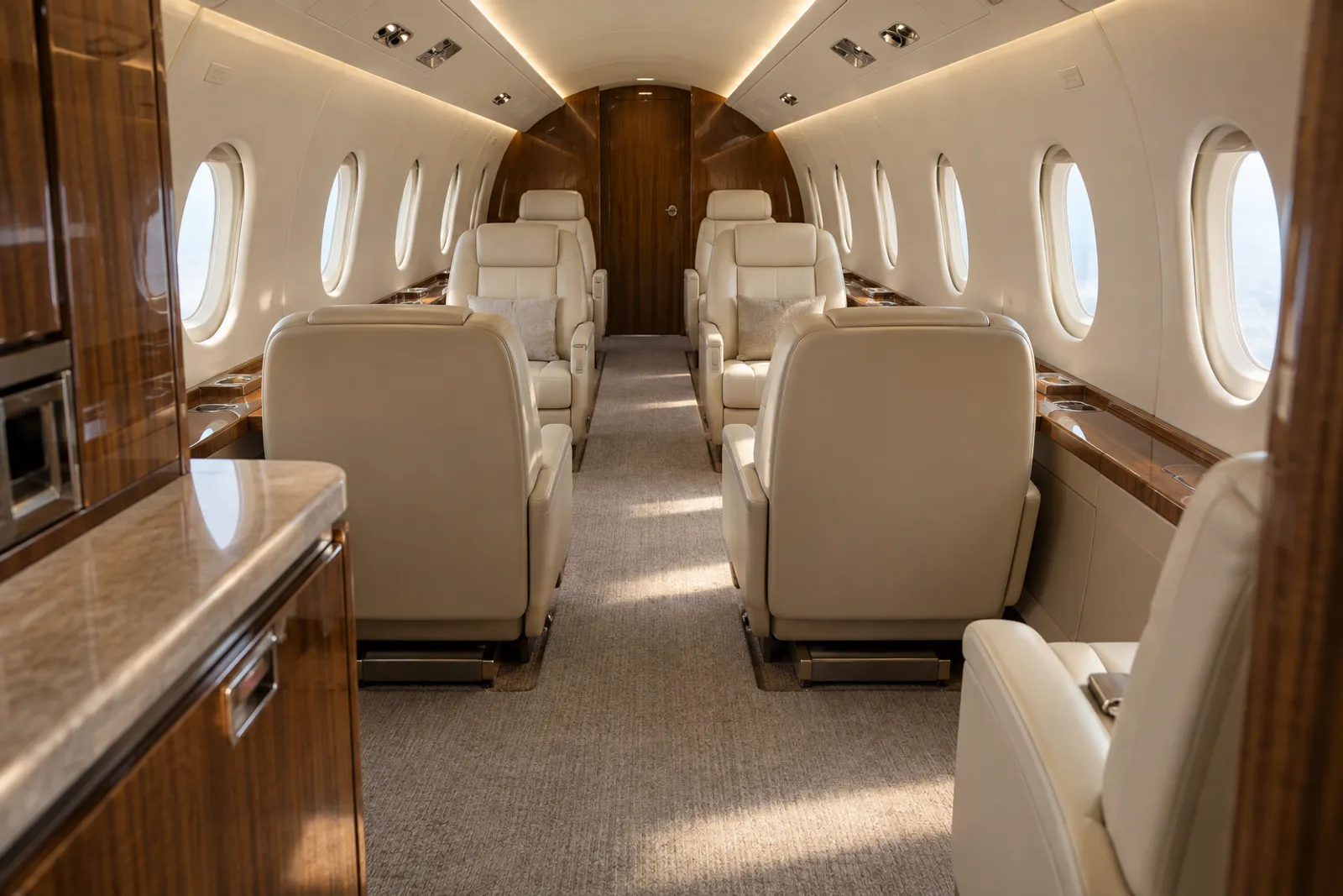 An eye-level view looking aft through an Embraer Praetor 500 cabin shows cream leather executive seats, warm wood veneer, upright oval windows and a flat central aisle beneath a six-foot arched ceiling.