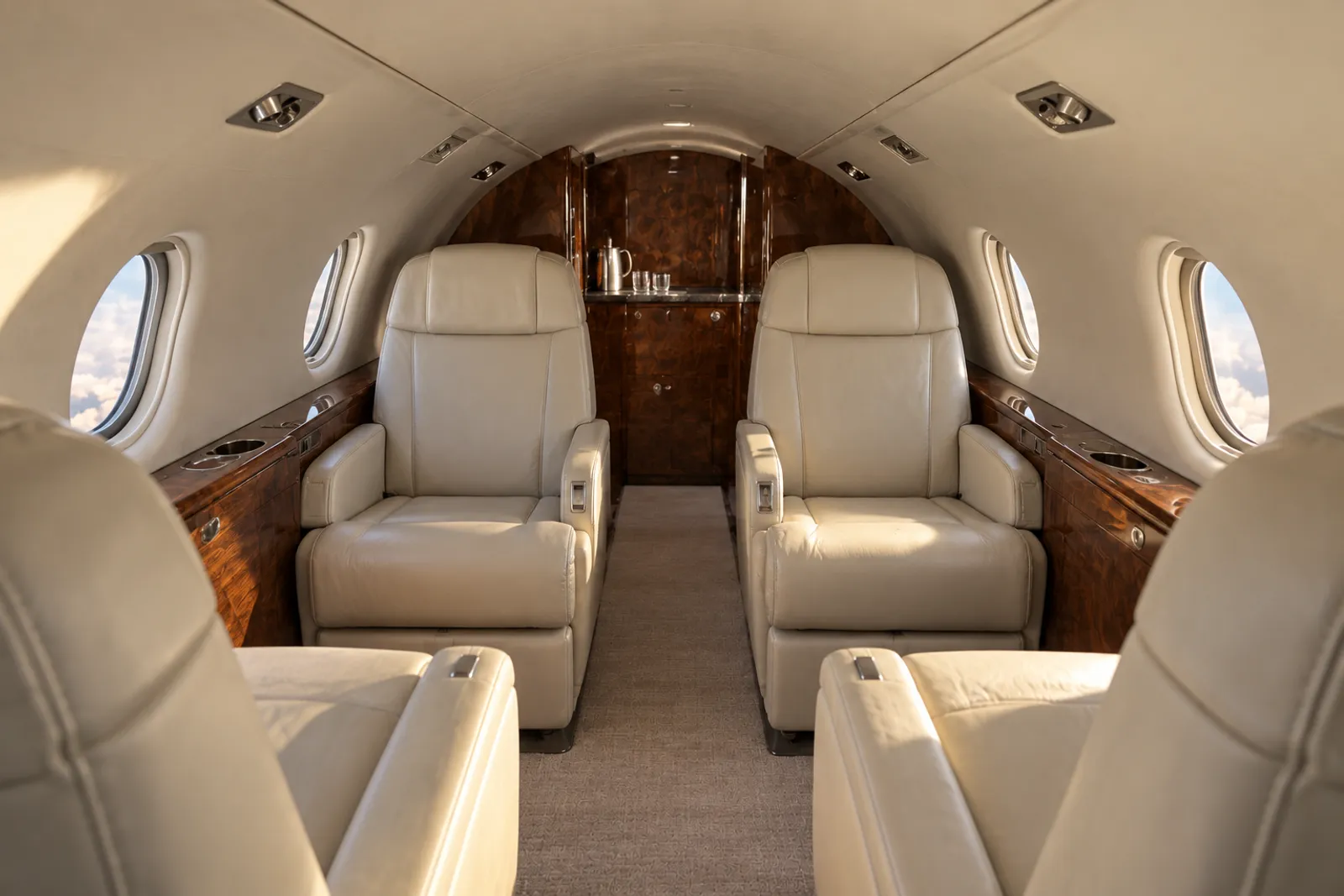Warm natural light fills the low, narrow Westwind II cabin with cream leather club chairs, a three-place side-facing divan, compact rounded windows, wood cabinetry and an aft lavatory door.